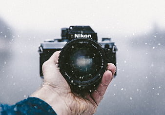 Hand holding vintage Nikon camera in snowy winter