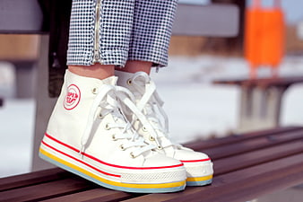 White high-top sneakers with colorful soles on a wooden bench
