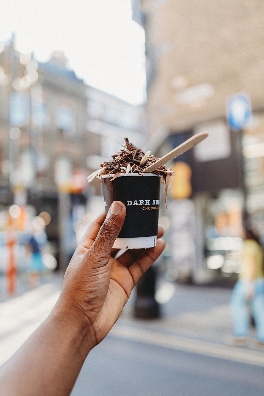 Hand holding dark chocolate ice cream cup on city street