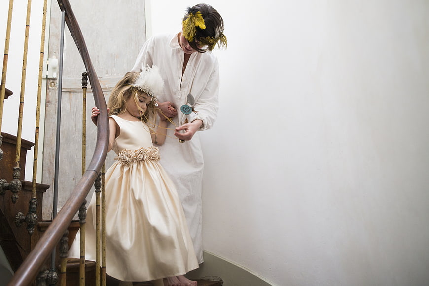 Mother and daughter in white dresses and feather masks on stairs