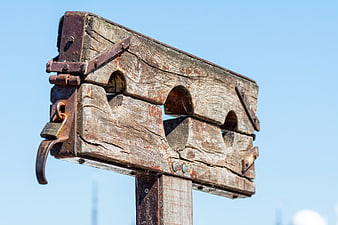Weathered wooden gallows structure against clear blue sky