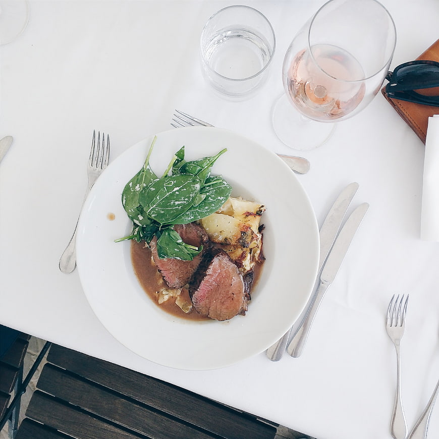 Top view of medium rare steak with spinach and potatoes on white table