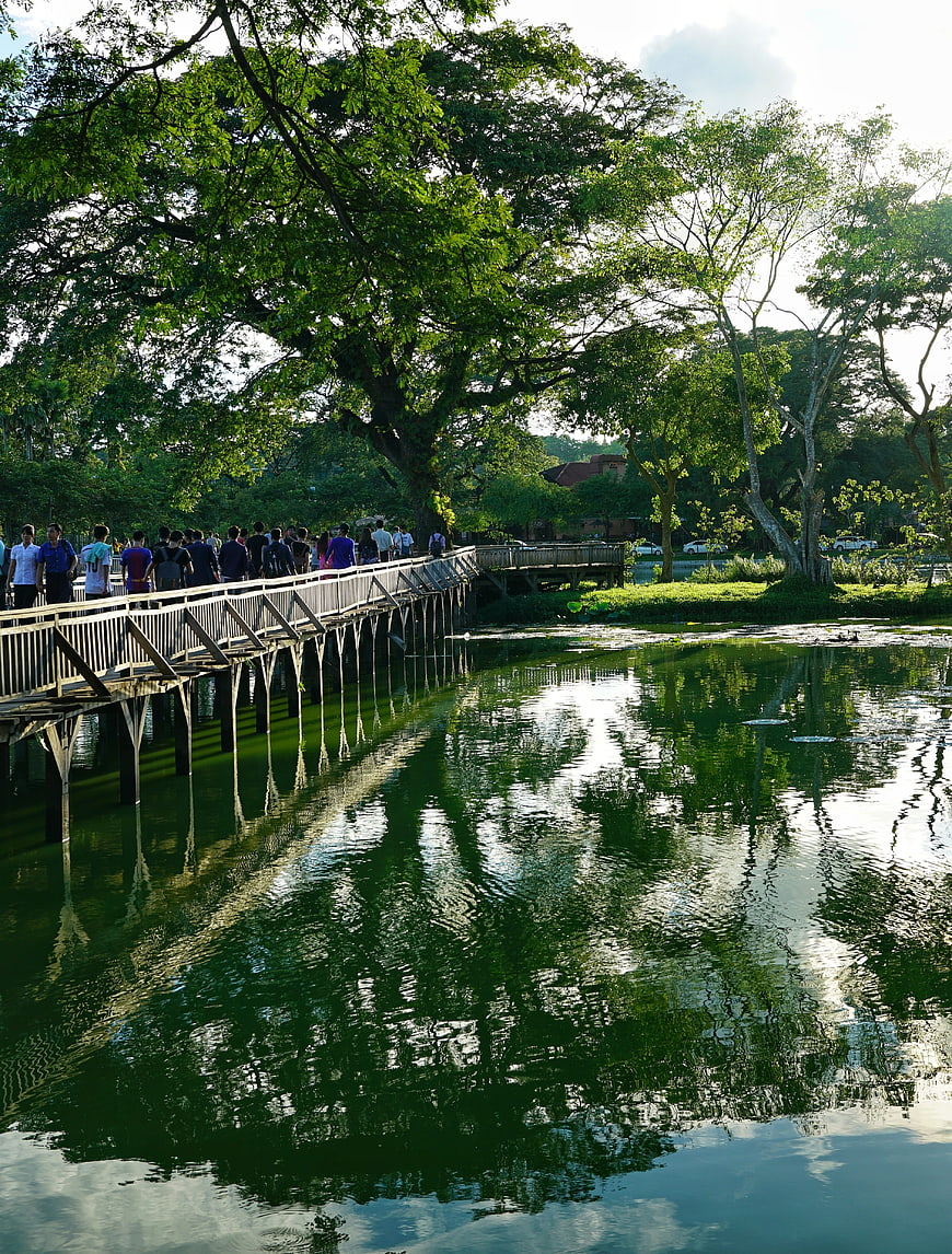 Crowd walking on wooden bridge over lake in Yangon park