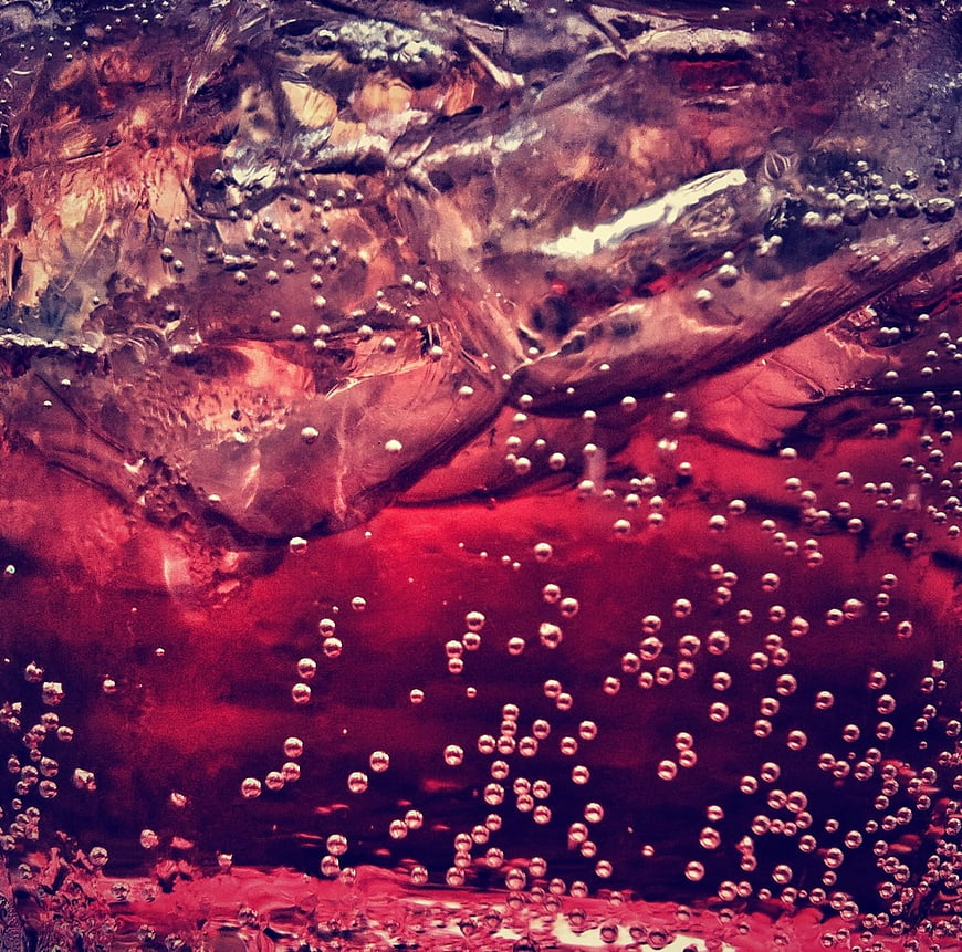 Macro shot of red carbonated drink with ice cubes and bubbles