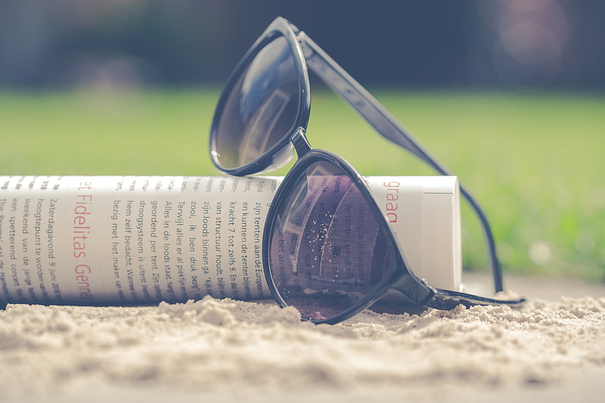 Sunglasses on Rolled Magazine on Sand Beach