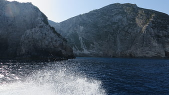 Boat wake splashing in deep blue sea near rocky cliffs