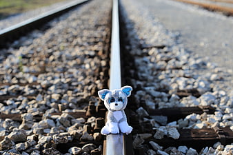 Small gray plush toy sitting on a railway track
