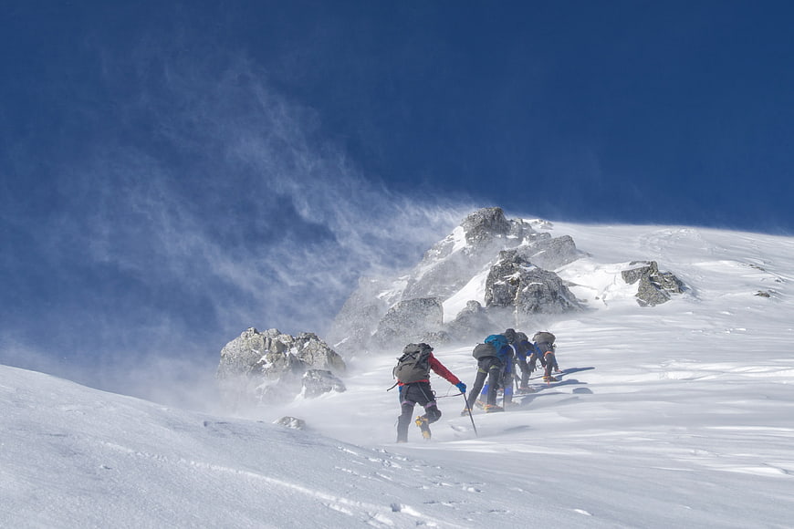 Mountain climbers ascending snowy peak in strong wind