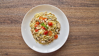 Overhead shot of spaghetti with mushrooms, cherry tomatoes, and basil on a white plate