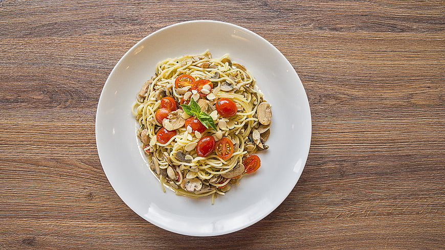 Overhead shot of spaghetti with mushrooms, cherry tomatoes, and basil on a white plate