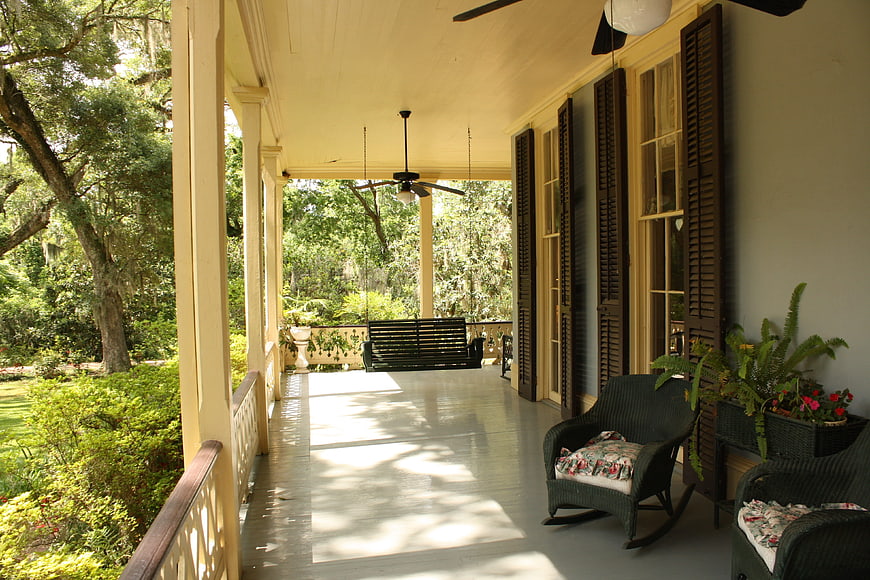 Southern Plantation Porch With Wicker Chairs And Lush Green Garden