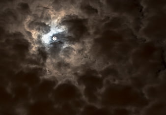Full moon glowing through dark storm clouds at night