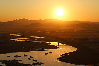 Golden Sunrise Over Winding River With Boats And Distant Mountains