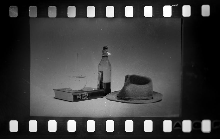 Vintage black and white still life with hat, bottle, and book