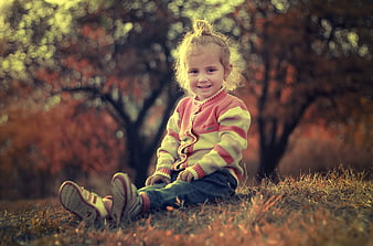 Cute little girl sitting in autumn park with colorful sweater