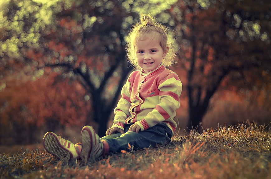 Cute little girl sitting in autumn park with colorful sweater