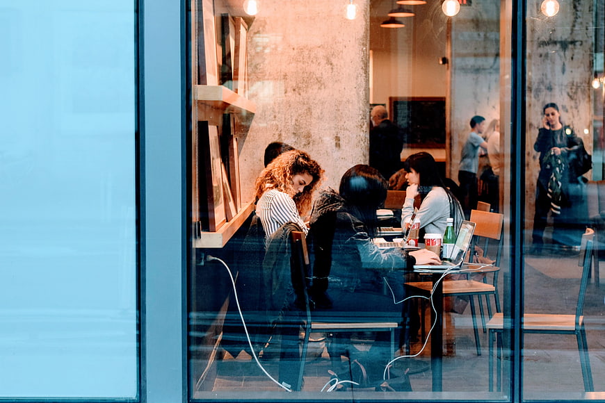 People working on laptops in a modern cafe seen through a window