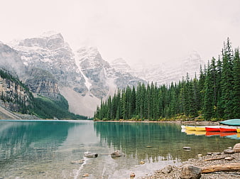 Serene turquoise lake with colorful canoes and misty mountains