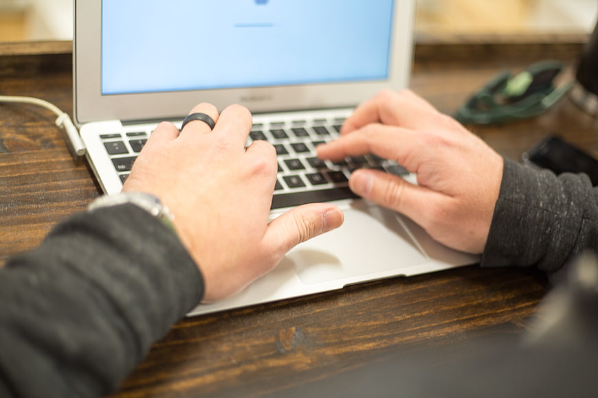 Close-up of hands typing on a laptop keyboard at a wooden desk