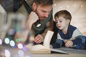 Father and son reading book with flashlight indoors