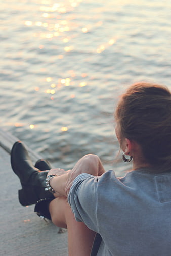 Woman sitting by water at sunset