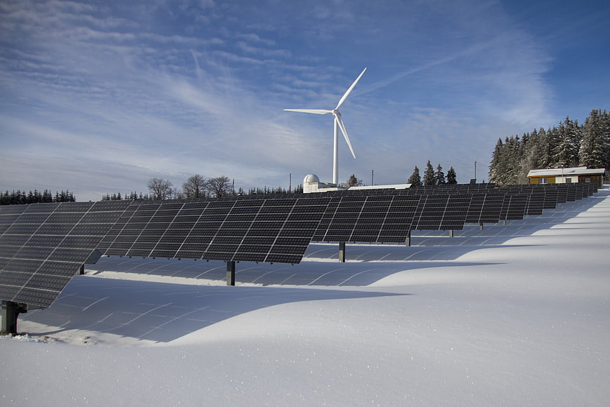 Solar panels and wind turbine on a snowy roof