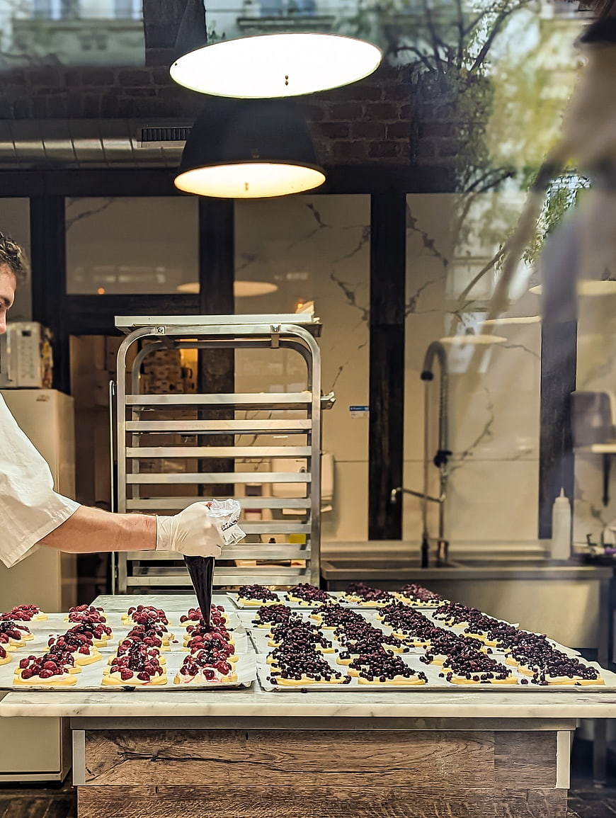 Chef piping chocolate ganache on berry tarts in bakery