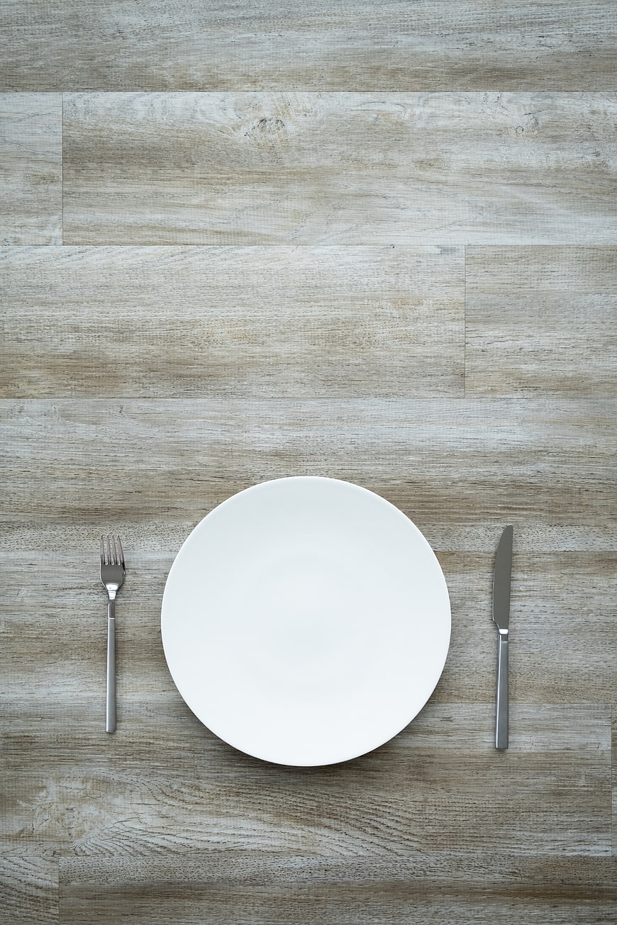 Minimalist white plate and silverware on rustic wooden table