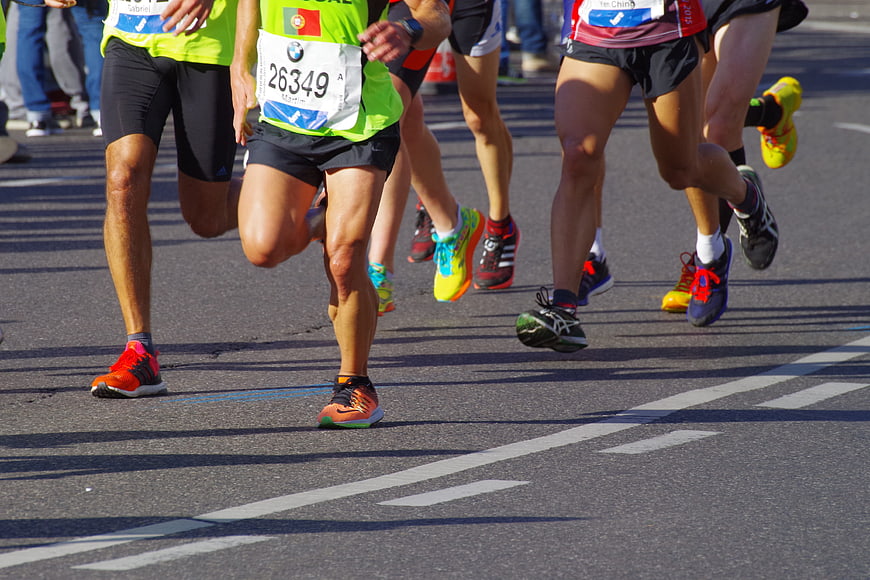 Marathon runners legs and colorful running shoes on asphalt road