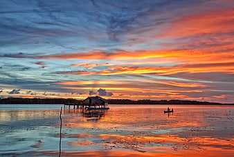 Vibrant sunset over lake with stilt house and canoe