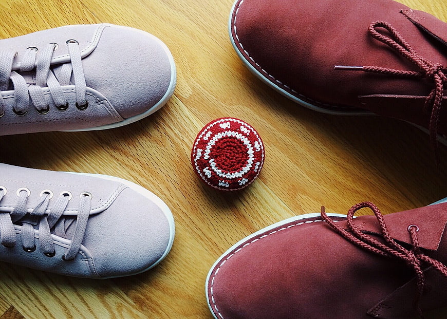 Two pairs of sneakers and a hacky sack on wooden floor