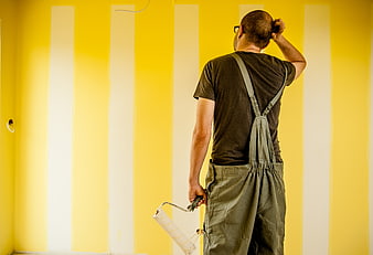Painter scratching head while renovating yellow striped wall