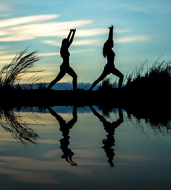 Silhouettes of Two Women Doing Yoga by Water at Sunset