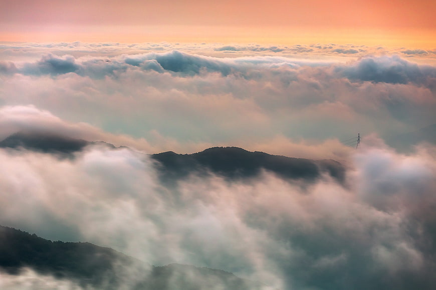 Misty mountain peaks emerging from sea of clouds at sunrise