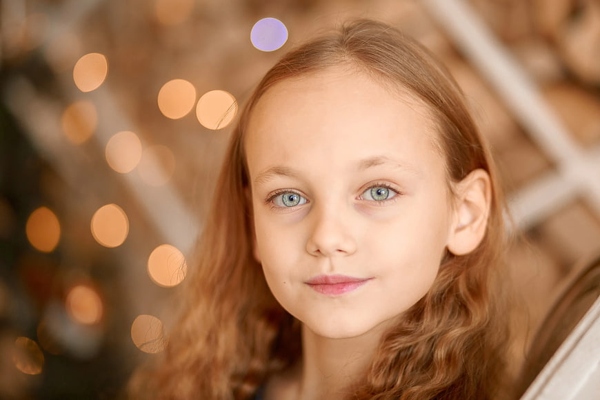 Close-up portrait of a young girl with blue eyes and bokeh lights