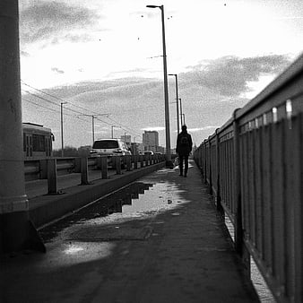 Solitary figure walking on urban bridge in black and white