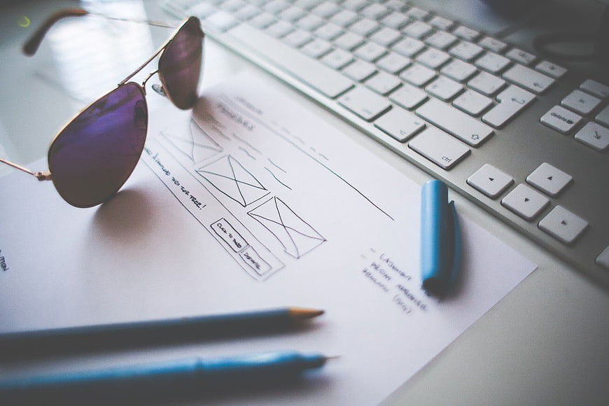 UX Design Sketches with Keyboard and Sunglasses on Desk