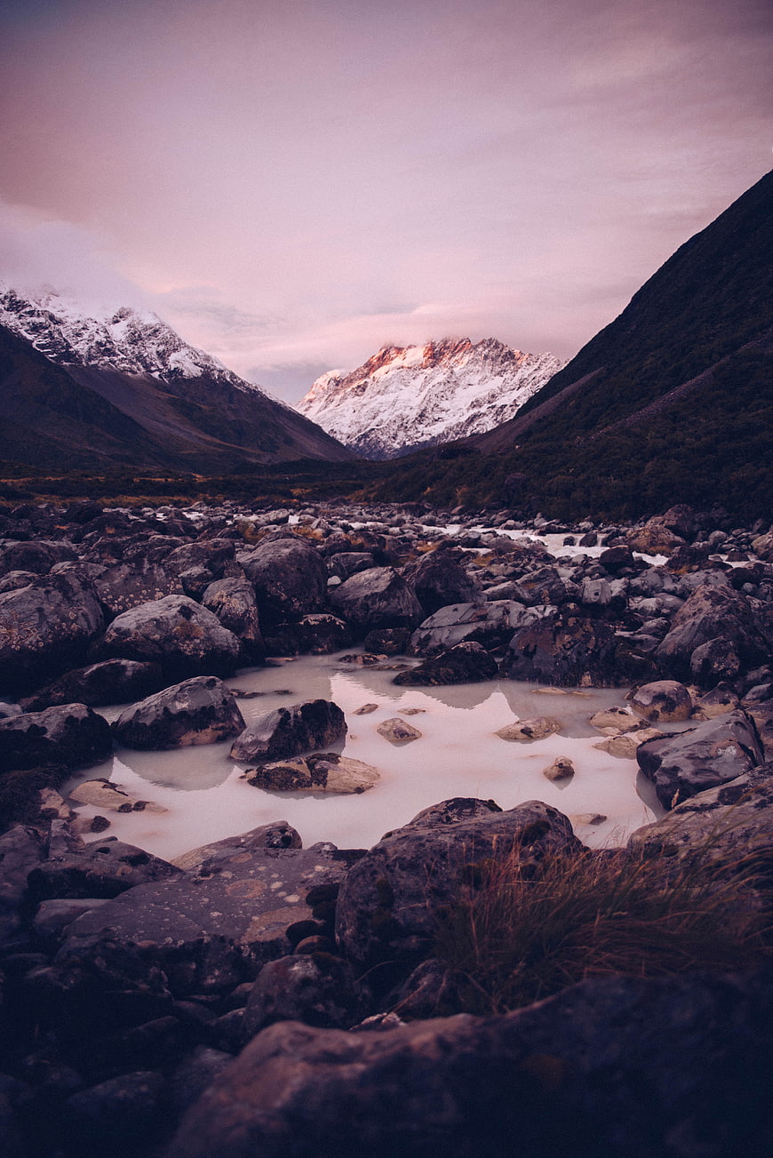 Snowy mountain peak at sunset with rocky riverbed