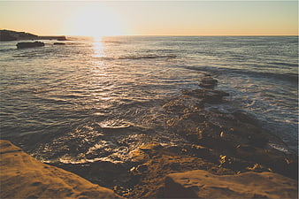 Golden Sunset Over Rocky Ocean Shoreline with Distant Cliff