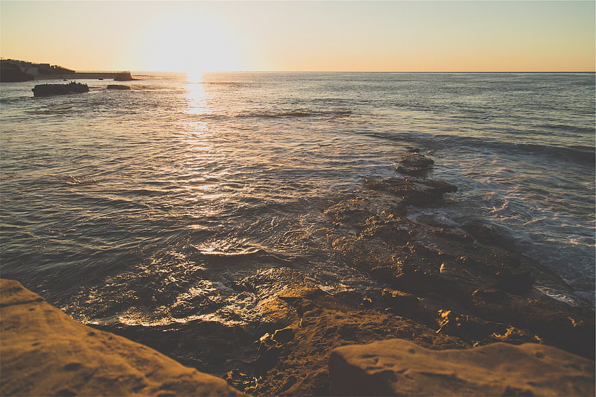 Golden Sunset Over Rocky Ocean Shoreline with Distant Cliff