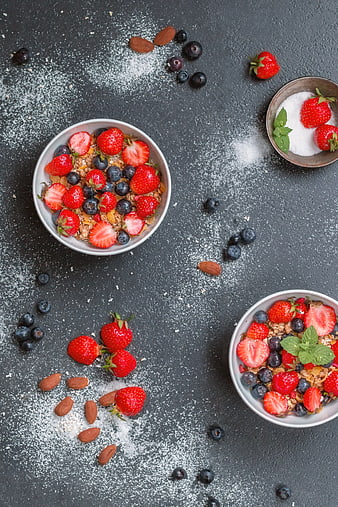Overhead view of healthy granola bowls with fresh strawberries and blueberries