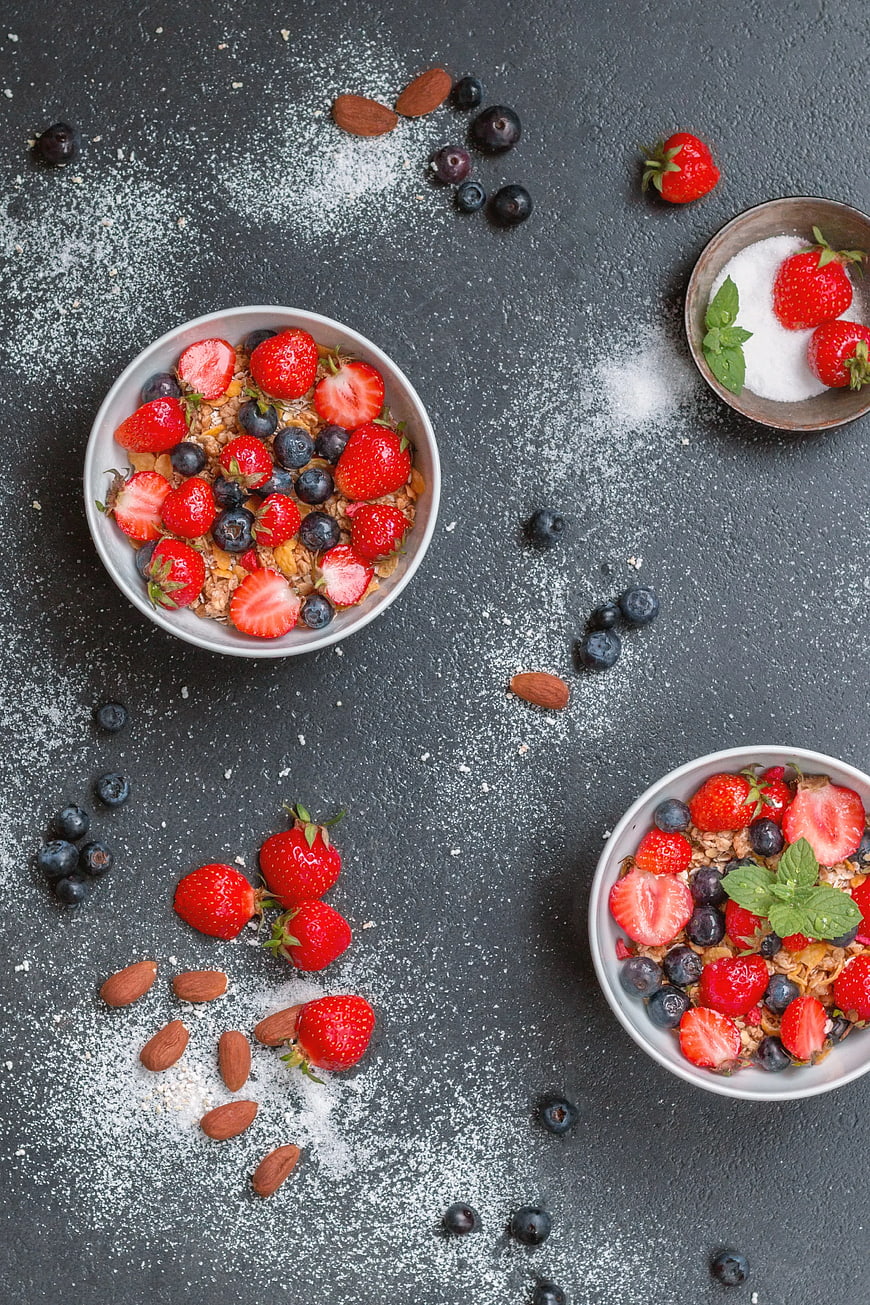 Overhead view of healthy granola bowls with fresh strawberries and blueberries