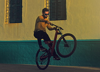 Man performing wheelie on mountain bike against yellow wall