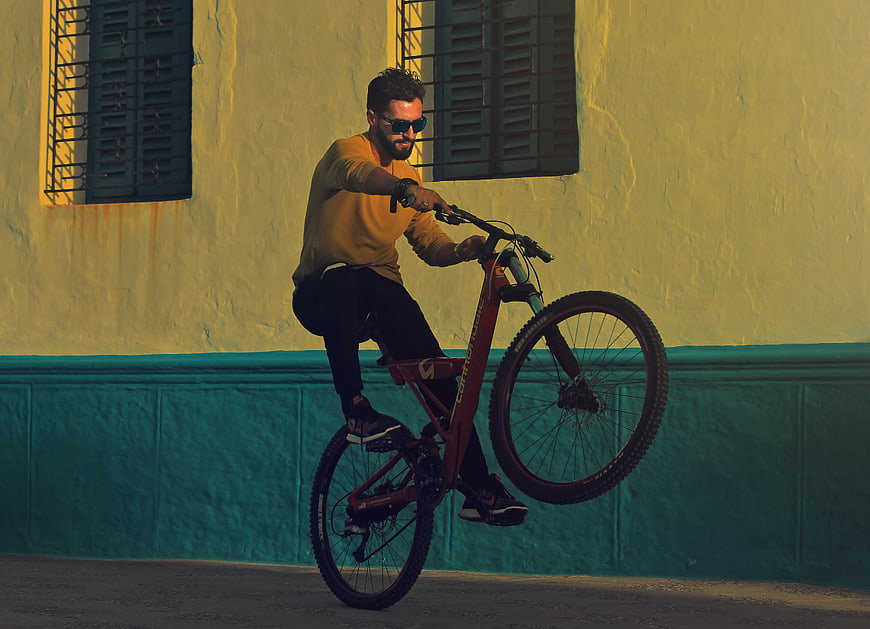 Man performing wheelie on mountain bike against yellow wall