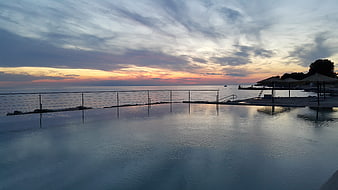 Serene infinity pool overlooking ocean sunset with dramatic clouds