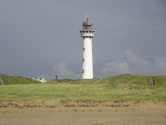 White Lighthouse on Grassy Dunes Under Stormy Sky