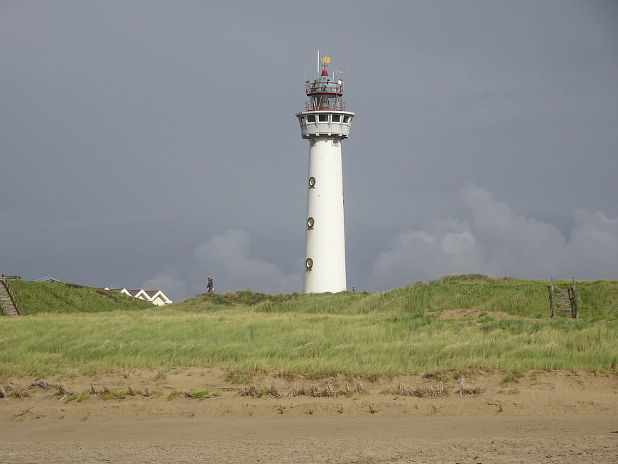 White Lighthouse on Grassy Dunes Under Stormy Sky