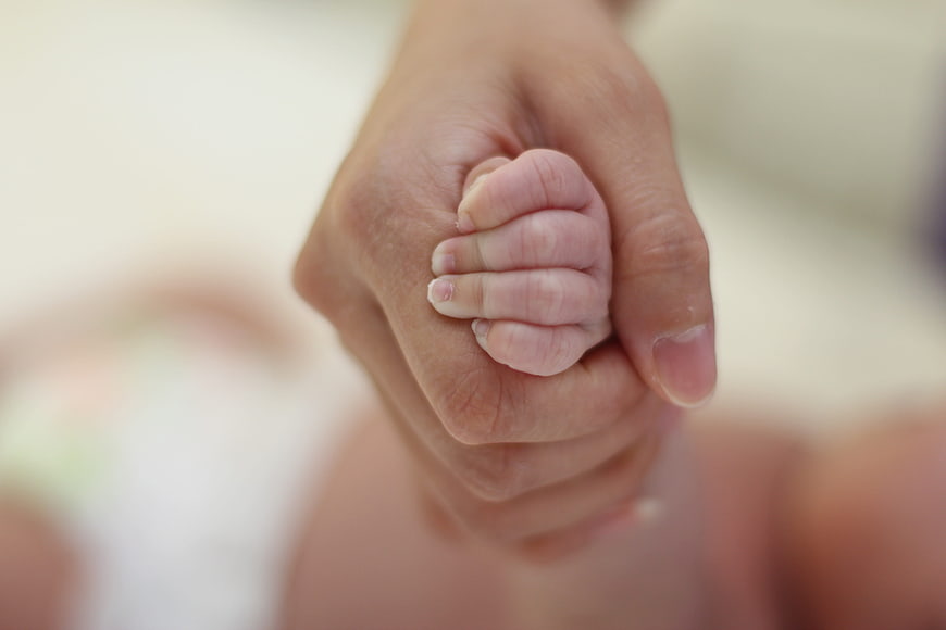 Close-up of adult hand holding baby's tiny hand