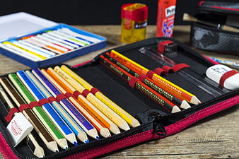 Colorful pencils in a red pencil case on a wooden table