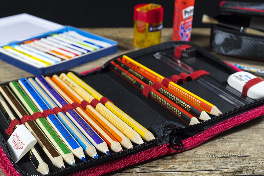 Colorful pencils in a red pencil case on a wooden table
